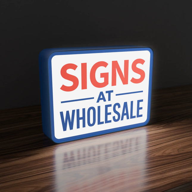 On Rectangular lit-shape lightbox sign displaying the text 'SIGNS AT WHOLESALE' in bold red and blue on a solid royal blue background, shown as a color swatch mockup
