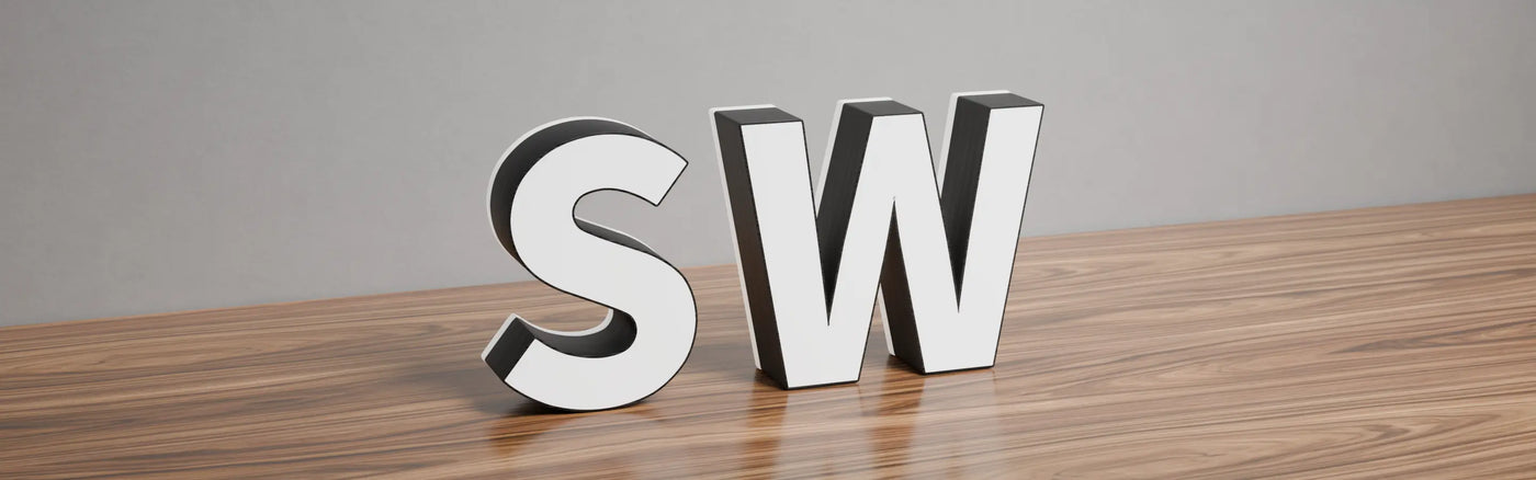 Face and edge lit 3D letters 'S' and 'W' with white faces and black sides, unilluminated and placed on a wooden surface with a plain grey background.