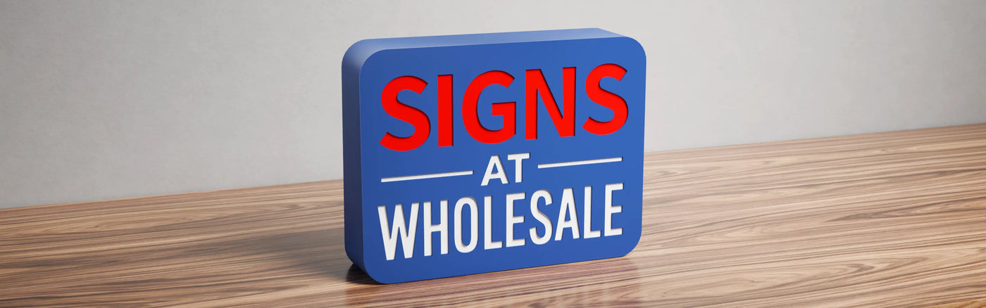 Off fret cut tray lightbox sign with raised red 'SIGNS' and white 'AT WHOLESALE' letters on a blue background, displayed on a wooden surface against a grey wall