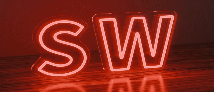 RGB neon sign displaying the letters SW glowing in multicolour, placed on a wooden surface with a dark background