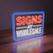 On uv-printed neon sign reading 'SIGNS AT WHOLESALE' on a wooden surface