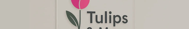 Clear acrylic sign with a pink tulip graphic and Tulips & More text, mounted on a wall with silver standoffs