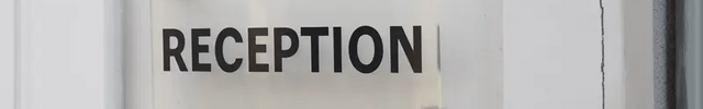 Clear acrylic sign with black 'Reception' text mounted on a white wall