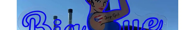 UV printed neon sign of a flexing woman with 'Jeep Girl' tattoo, wearing a headband with a Puerto Rican flag, and the words 'Big ue' in blue script against a clear sky background