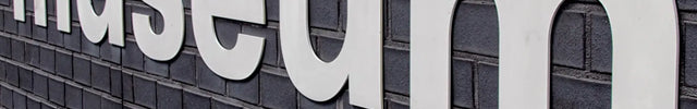 Large white acrylic letters spelling museum mounted on a dark brick wall for outdoor signage